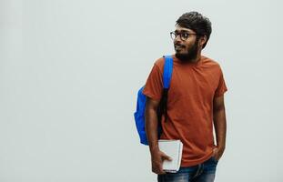 Indian student with blue backpack, glasses and notebook posing on gray background. The concept of education and schooling. Time to go back to school photo