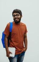 Indian student with blue backpack, glasses and notebook posing on gray background. The concept of education and schooling. Time to go back to school photo
