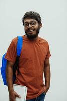 indio estudiante con azul mochila, lentes y cuaderno posando en gris antecedentes. el concepto de educación y enseñanza. hora a Vamos espalda a colegio foto