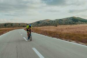 Full length portrait of an active triathlete in sportswear and with a protective helmet riding a bicycle. Selective focus photo