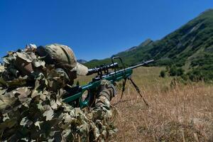 Army soldier holding sniper rifle with scope and aiming in forest. War, army, technology and people concept photo