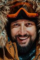 Head shot of a man in a cold snowy area wearing a thick brown winter jacket, snow goggles and gloves on a cold Scandinavian night. Life in the cold regions of the country. photo