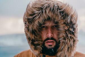 Headshot photo of a man in a cold snowy area wearing a thick brown winter jacket and gloves. Life in cold regions of the country.