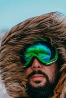 disparo a la cabeza foto de un hombre en un frío Nevado zona vistiendo un grueso marrón invierno chaqueta, nieve gafas de protección y guantes. vida en frío regiones de el país.