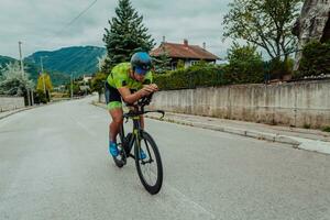 lleno longitud retrato de un activo triatleta en ropa de deporte y con un protector casco montando un bicicleta. selectivo atención foto