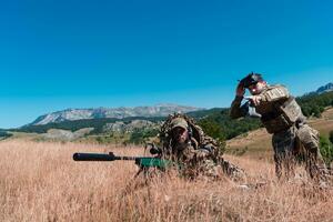 Sniper soldier assisted by an assistant to observe the area to be targeted with modern warfare tactical virtual reality goggles aerial drone military technology. photo