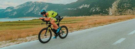 lleno longitud retrato de un activo triatleta en ropa de deporte y con un protector casco montando un bicicleta. selectivo atención foto