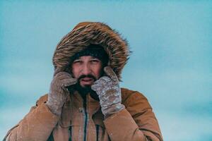 disparo a la cabeza foto de un hombre en un frío Nevado zona vistiendo un grueso marrón invierno chaqueta y guantes. vida en frío regiones de el país.