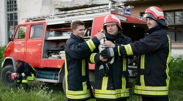 firefighters group in a protective suit and red helmet holds saved cat in his arms. Firefighter in fire fighting operation. photo