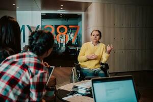 Businesswoman in wheelchair having business meeting with team at modern office. A group of young freelancers agree on new online business projects photo