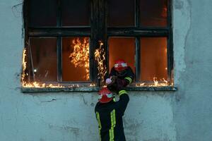 bombero héroe que lleva bebé niña fuera desde ardiente edificio zona desde fuego incidente. rescate personas desde peligroso sitio foto