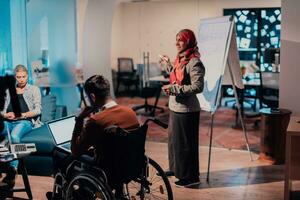 An older Muslim businesswoman presents a project to a young diverse team of people in a modern office photo