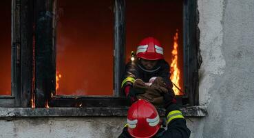 Firefighter hero carrying baby girl out from burning building area from fire incident. Rescue people from dangerous place photo