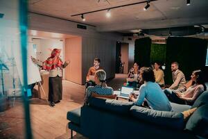 An older Muslim businesswoman presents a project to a young diverse team of people in a modern office photo