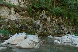 A military man or airsoft player in a camouflage suit sneaking the river and aims from a sniper rifle to the side or to target. photo