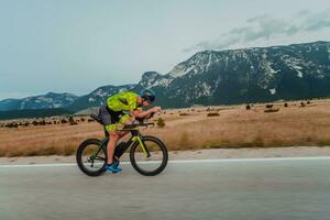 lleno longitud retrato de un activo triatleta en ropa de deporte y con un protector casco montando un bicicleta. selectivo atención foto