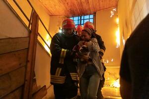 Brave Fireman Descends Stairs of a Burning Building and Holds Saved Girl in His Arms. Open fire and one Firefighter in the Background. photo