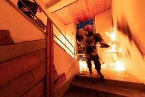 valiente bombero desciende escalera de un ardiente edificio y sostiene salvado niña en su brazos. abierto fuego y uno bombero en el antecedentes. foto