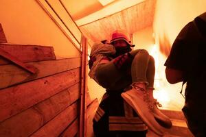 Brave Fireman Descends Stairs of a Burning Building and Holds Saved Girl in His Arms. Open fire and one Firefighter in the Background. photo