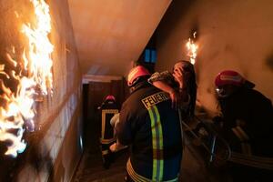 valiente bombero desciende escalera de un ardiente edificio y sostiene salvado niña en su brazos. abierto fuego y uno bombero en el antecedentes. foto