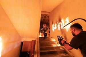 Brave Fireman Descends Stairs of a Burning Building and Holds Saved Girl in His Arms. Open fire. Cinematographer taking shoot with pro cinema camera and three-axis gimbal stabilization. low light photo