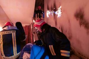 Brave Fireman Descends Stairs of a Burning Building and Holds Saved Girl in His Arms. Open fire and one Firefighter in the Background. photo