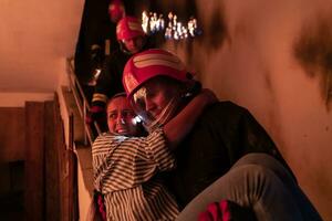 Brave Fireman Descends Stairs of a Burning Building and Holds Saved Girl in His Arms. Open fire and one Firefighter in the Background. photo