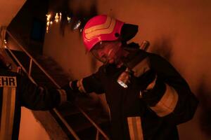 Brave Fireman Descends Stairs of a Burning Building and Holds Saved Girl in His Arms. Open fire and one Firefighter in the Background. photo