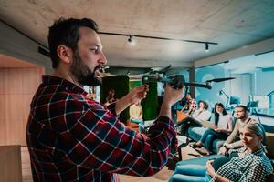 un barbado hombre en un moderno oficina explicando a su joven diverso equipo cómo un zumbido trabajando foto