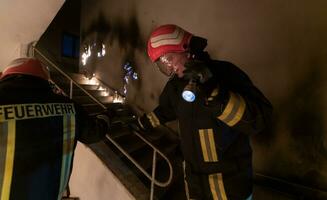 Brave Fireman Descends Stairs of a Burning Building and Holds Saved Girl in His Arms. Open fire and one Firefighter in the Background. photo