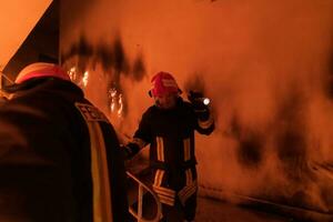 Brave Fireman Descends Stairs of a Burning Building and Holds Saved Girl in His Arms. Open fire and one Firefighter in the Background. photo