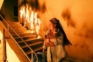 Brave Fireman Descends Stairs of a Burning Building and Holds Saved Girl in His Arms. Open fire and one Firefighter in the Background. photo