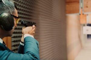 A man practices shooting a pistol in a shooting range while wearing protective headphones photo