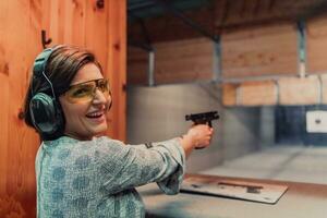 un mujer practicas disparo un pistola en un disparo rango mientras vistiendo protector auriculares foto