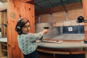 un mujer practicas disparo un pistola en un disparo rango mientras vistiendo protector auriculares foto