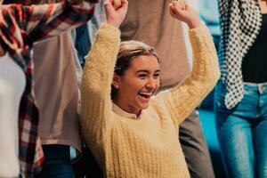 Photo of business women in wheelchairs with their hands raised in the air with their colleagues, together celebrating business success