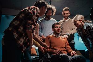 Colleagues help their friend in a wheelchair to take his first steps in a modern office after a serious illness photo