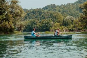 Couple adventurous explorer friends are canoeing in a wild river surrounded by the beautiful nature photo