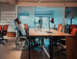 Businessman with a disability in wheelchair working overtime alone at his desk in an office late at night photo