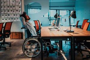 Businessman with a disability in wheelchair working overtime alone at his desk in an office late at night photo