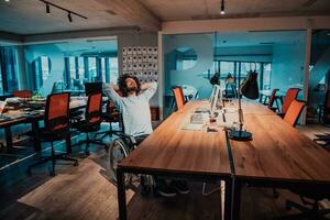 Businessman with a disability in wheelchair working overtime alone at his desk in an office late at night photo