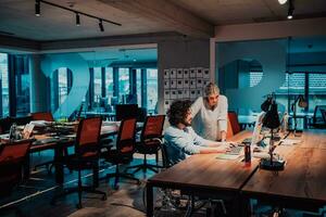 A businessman in a wheelchair in a modern coworking office space working with a female colleague late at nigh. Colleagues in the background photo