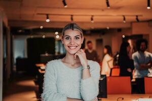 Portrait photo of a modern blonde on a break from work in a modern office. In the background, the team working on the projects