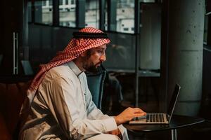 An elderly Arab man sitting in the office and analyzes data on his laptop photo