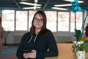 Portrait of happy multiethnic businesswoman using smartphone in agency. Successful business woman in casual clothing working in coworking creative open space office photo