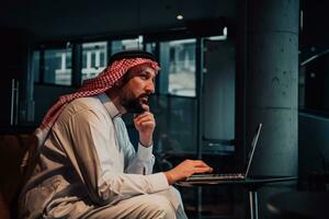 An elderly Arab man sitting in the office and analyzes data on his laptop photo