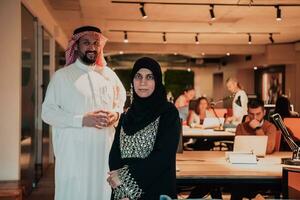 Portrait photo of Arab leader businessman with muslim hijab woman discussing business projects while using tablets and smartphone in modern glass office