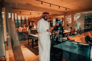 Portrait photo of Arab leader businessman with muslim hijab woman discussing business projects while using tablets and smartphone in modern glass office