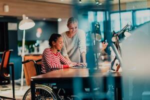 Businesswoman in a wheelchair working in a creative office. Business team in modern coworking office space. Colleagues working in the background at late night. photo