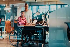 Businesswoman in a wheelchair working in a creative office. Business team in modern coworking office space. Colleagues working in the background at late night. photo